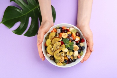 Photo of Woman with delicious exotic fruit salad on purple background, top view