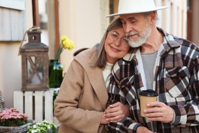 Affectionate senior couple drinking coffee outdoors, space for text