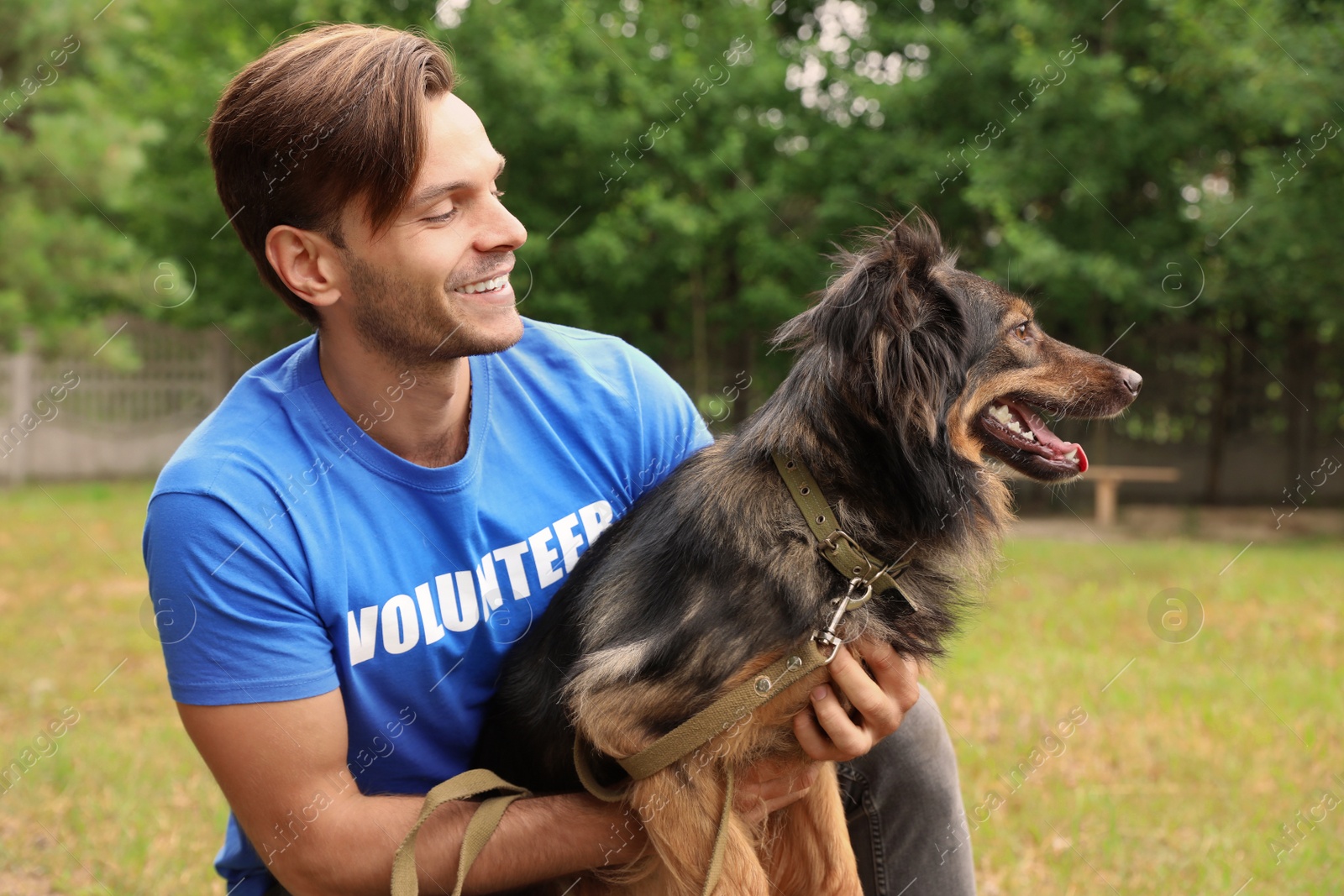 Photo of Male volunteer with homeless dog at animal shelter outdoors