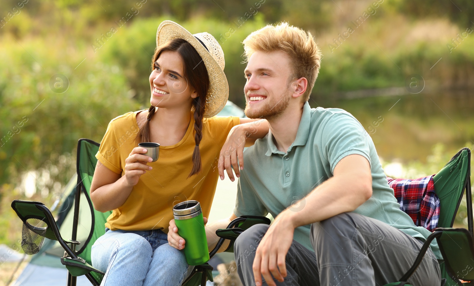 Photo of Young couple with hot drinks resting outdoors. Camping vacation