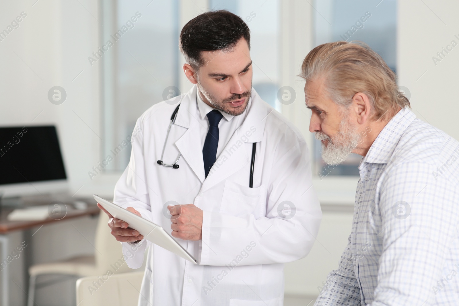 Photo of Doctor with tablet consulting senior patient in clinic