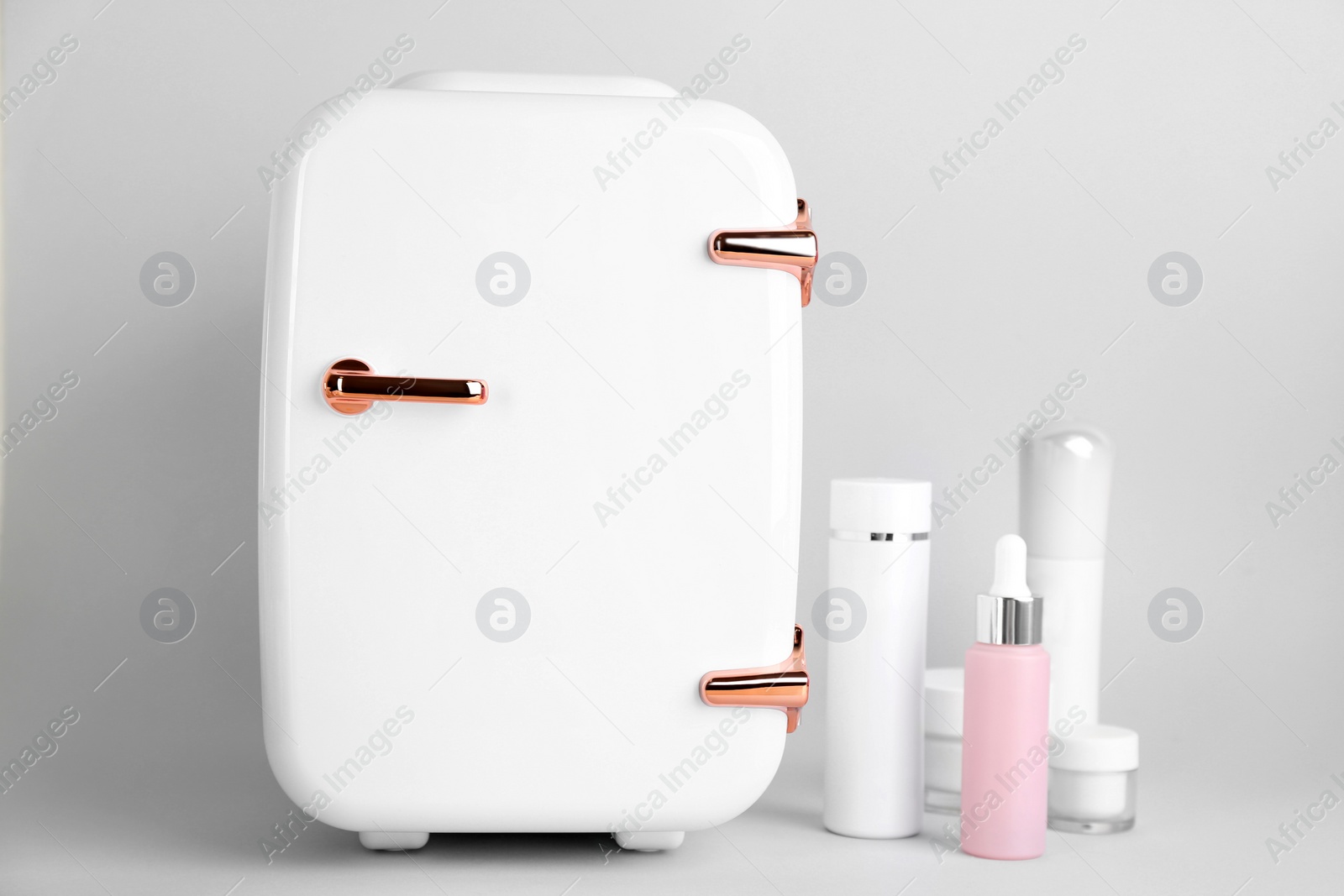 Photo of Cosmetic refrigerator and skin care products on light background