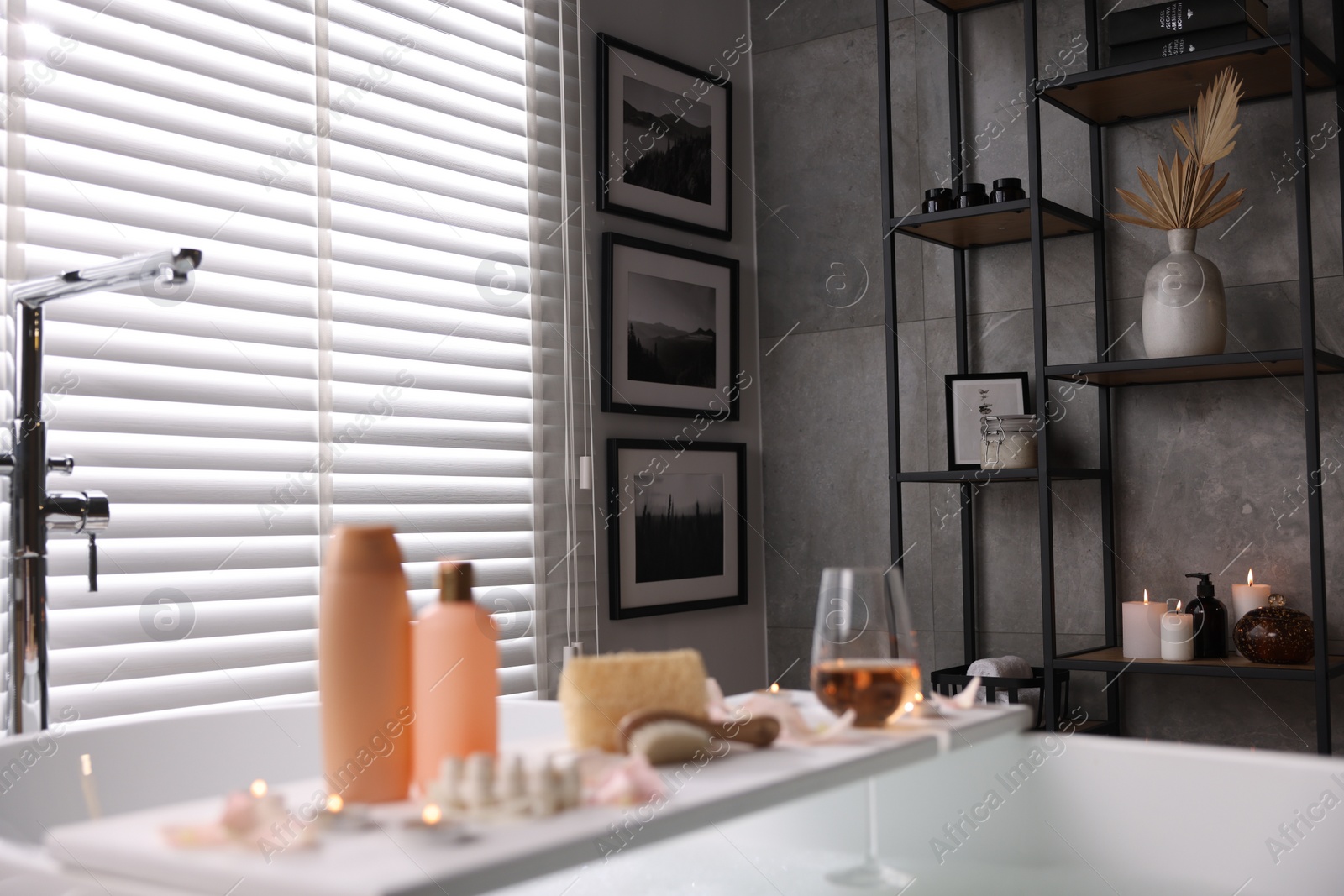 Photo of Wooden tray with wine, toiletries and flower petals on bathtub in bathroom, selective focus