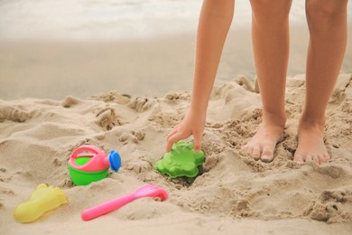 Photo of Little girl playing with plastic toys on sandy beach, closeup