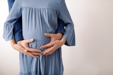 Young pregnant couple on light background, closeup of hands. Space for text