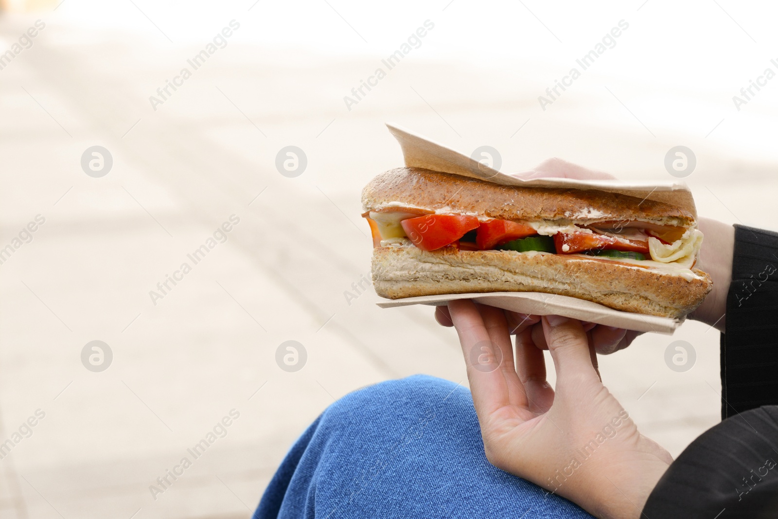 Photo of Woman holding tasty sandwich with vegetables outdoors, closeup and space for text. Street food