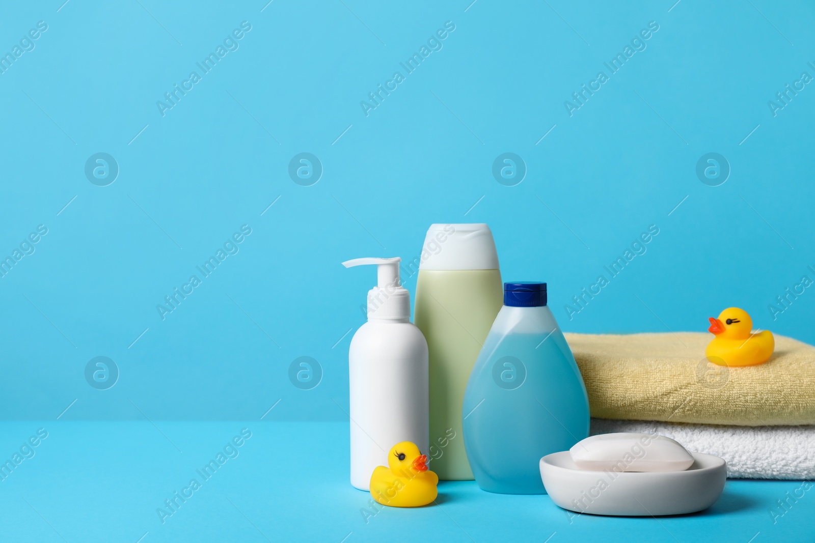 Photo of Baby cosmetic products, bath ducks and towels on light blue background. Space for text
