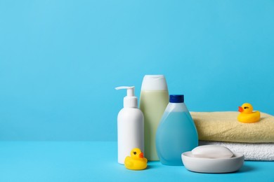 Photo of Baby cosmetic products, bath ducks and towels on light blue background. Space for text