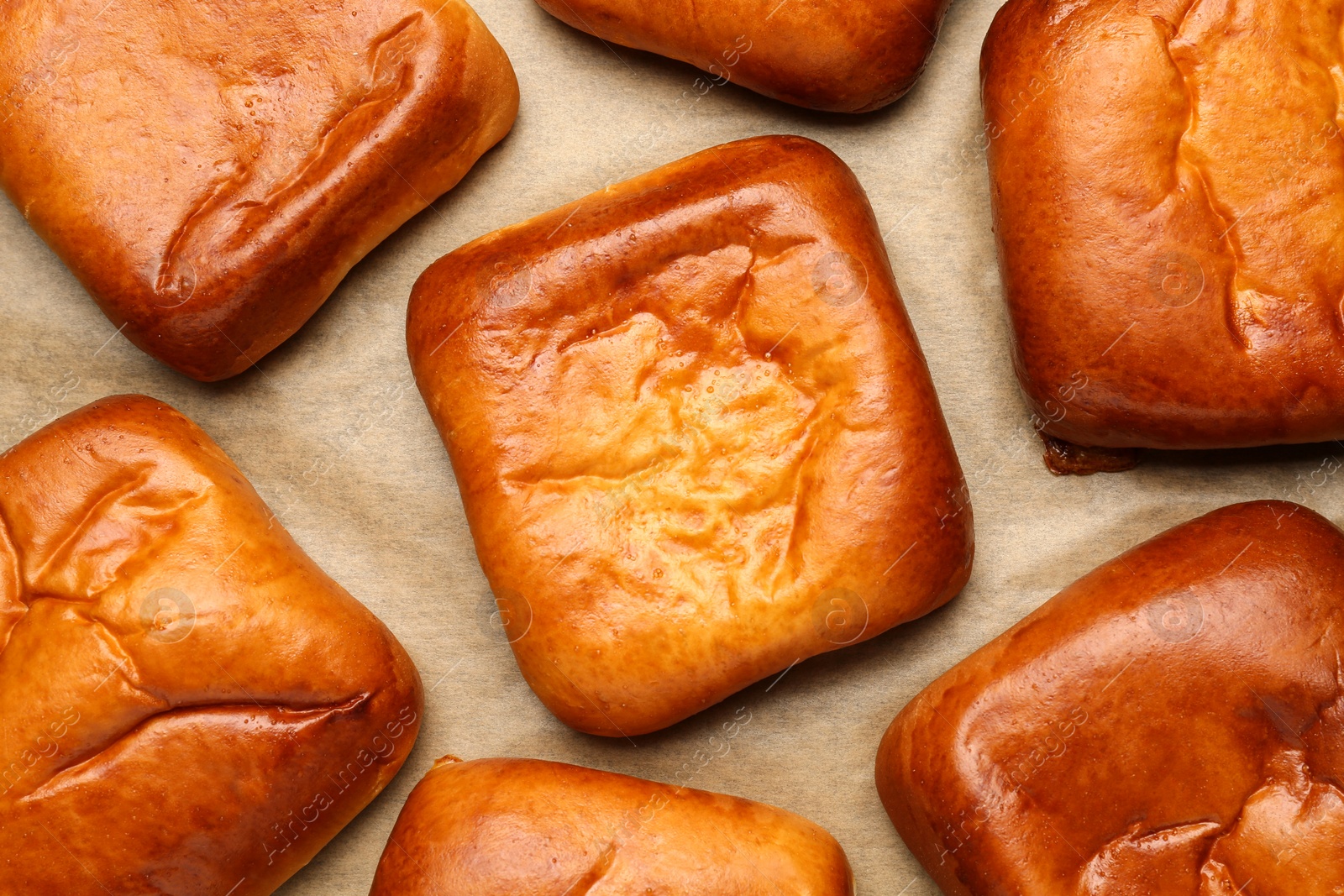 Photo of Many delicious baked patties on parchment paper, flat lay