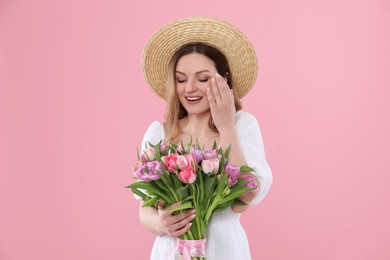 Photo of Happy young woman in straw hat holding bouquet of beautiful tulips on pink background
