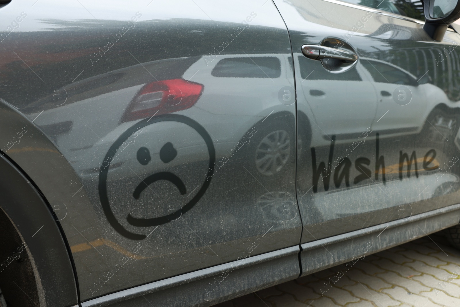 Photo of Phrase Wash Me and sad emoticon drawn on dirty car, closeup