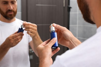 Photo of Handsome bearded man with bottle of oil in bathroom, closeup