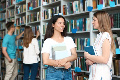 Photo of Young people standing near bookshelves in library