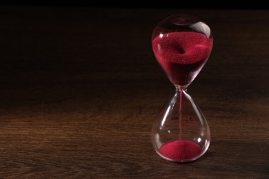 Photo of Hourglass with pink flowing sand on wooden table. Space for text