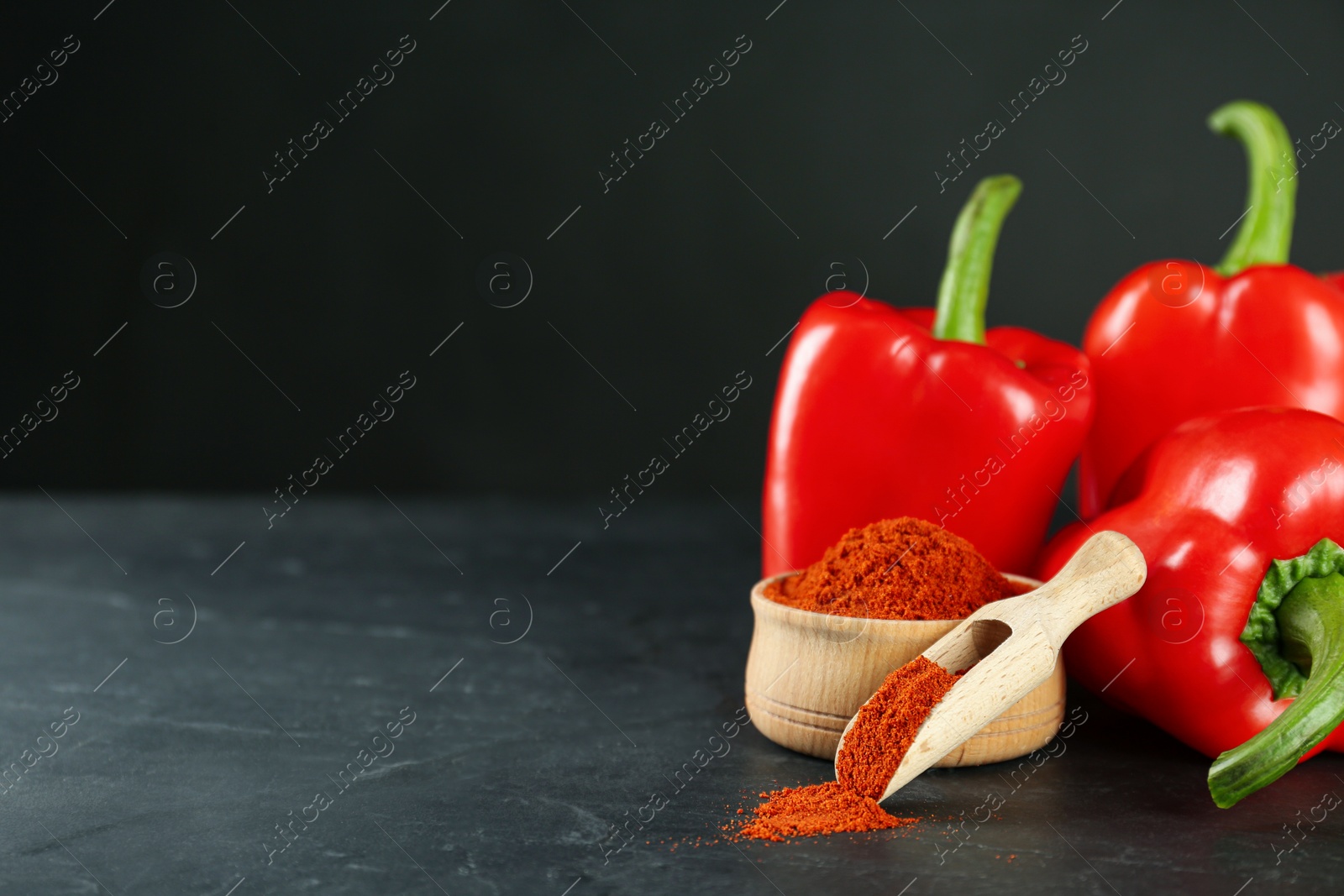 Photo of Paprika powder and fresh bell peppers on black table. Space for text
