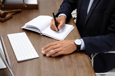 Photo of Male lawyer working with computer and notebook at table, closeup