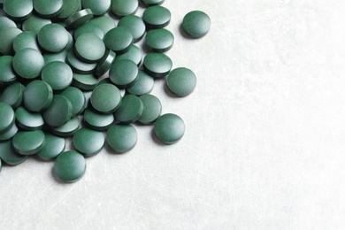 Photo of Heap of green spirulina pills on light table. Space for text