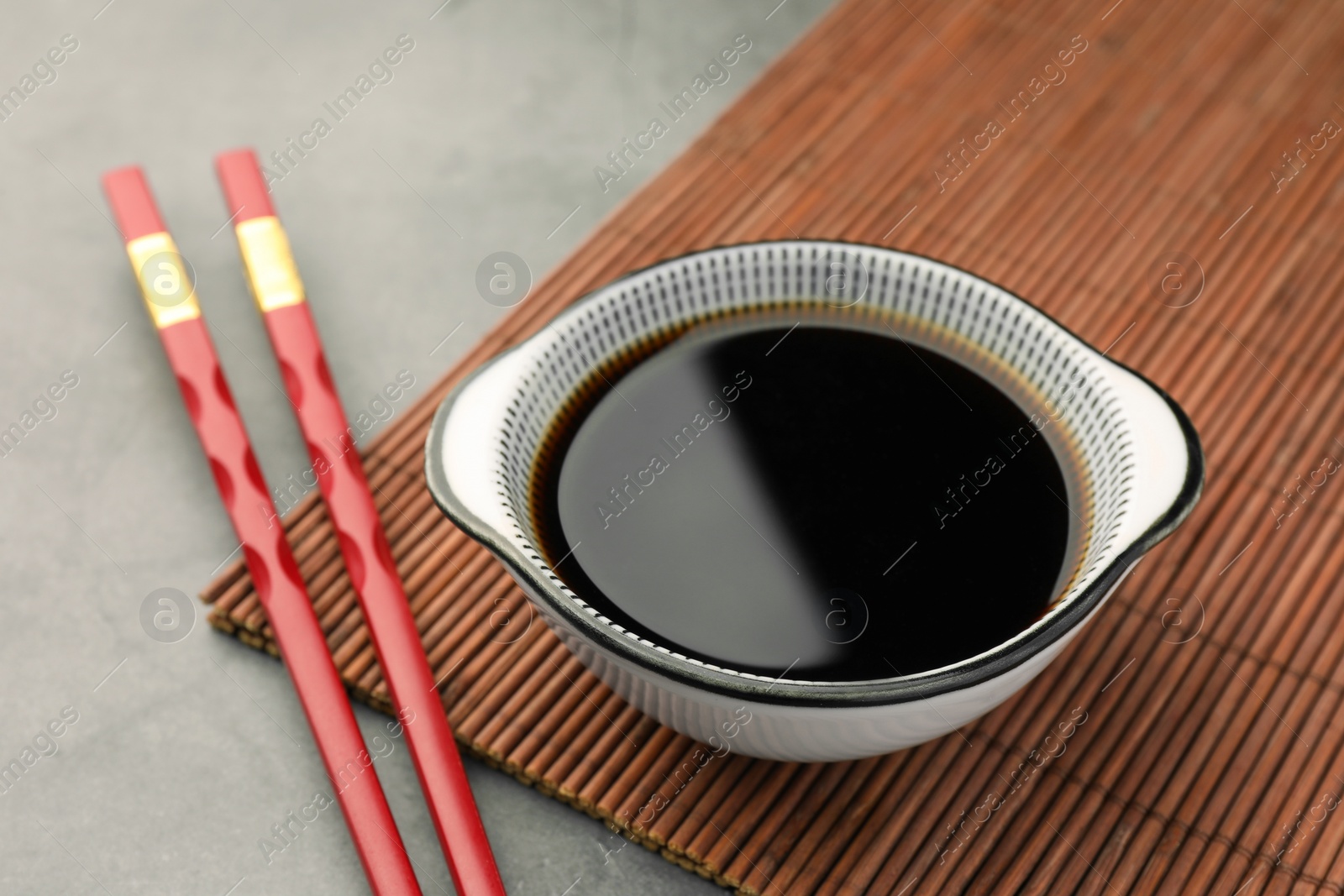 Photo of Bowl of soy sauce and chopsticks on grey table closeup