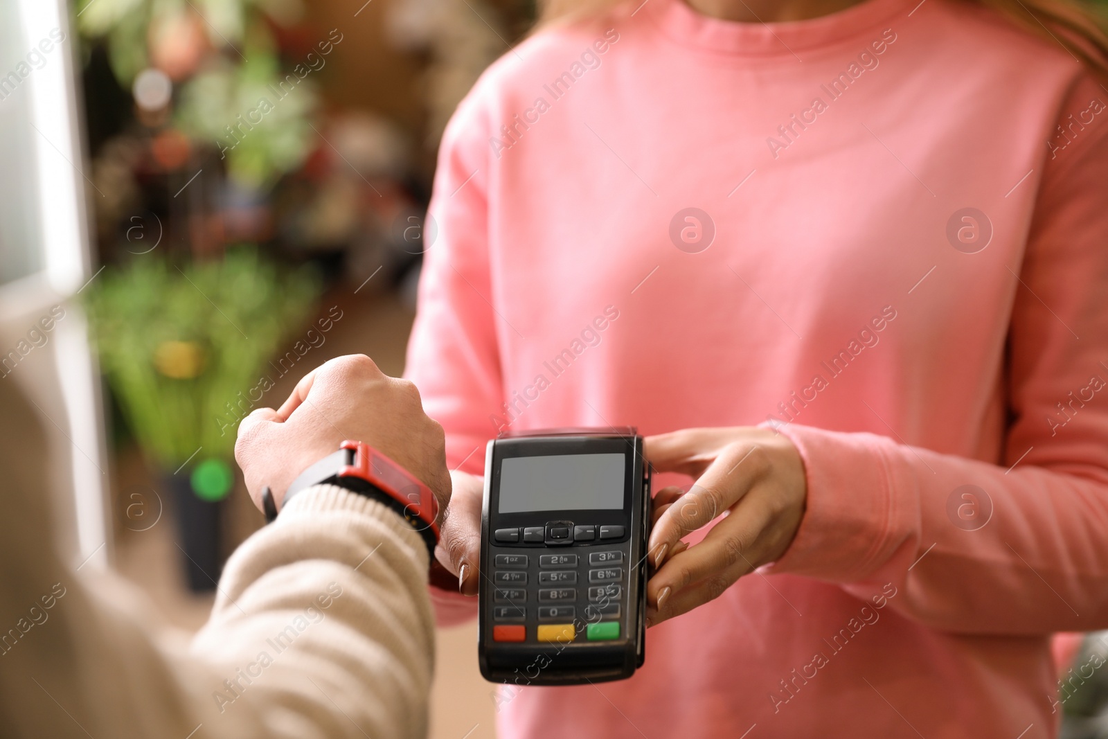 Photo of Customer using terminal for contactless payment with smartwatch in floral shop, closeup