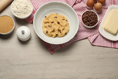 Photo of Fresh dough and different ingredients for cooking chocolate chip cookies on white wooden table, flat lay. Space for text