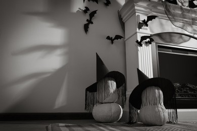 Photo of Beautiful black witch hats on pumpkins near fireplace indoors, space for text. Halloween celebration