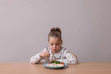 Photo of Cute little girl refusing to eat her dinner at table on grey background
