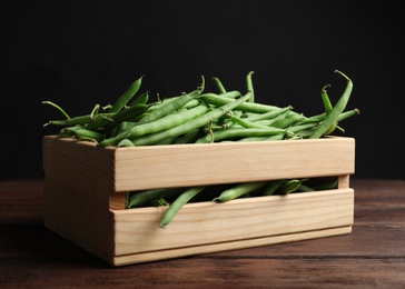 Fresh green beans in crate on wooden table against black background