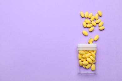 Photo of Tasty yellow dragee candies and container on lilac background, flat lay. Space for text