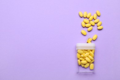 Tasty yellow dragee candies and container on lilac background, flat lay. Space for text