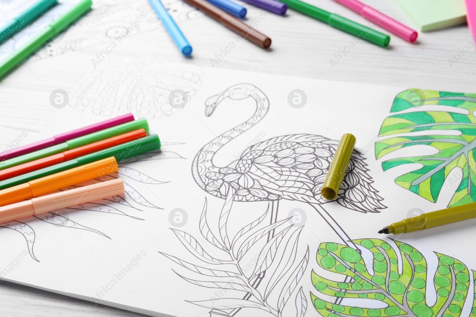 Photo of Antistress coloring page and felt tip pens on white wooden table, closeup