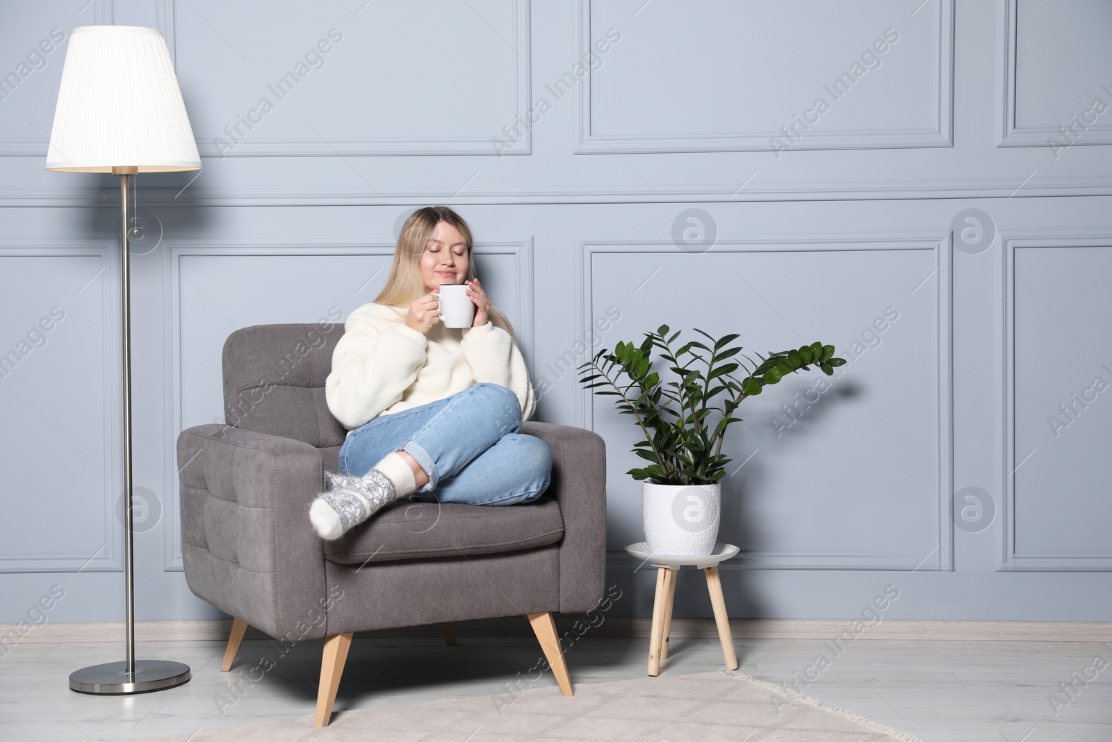 Photo of Young woman with cup of drink relaxing in armchair at home, space for text. Interior design