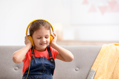 Photo of Cute little girl with headphones on sofa at home. Space for text