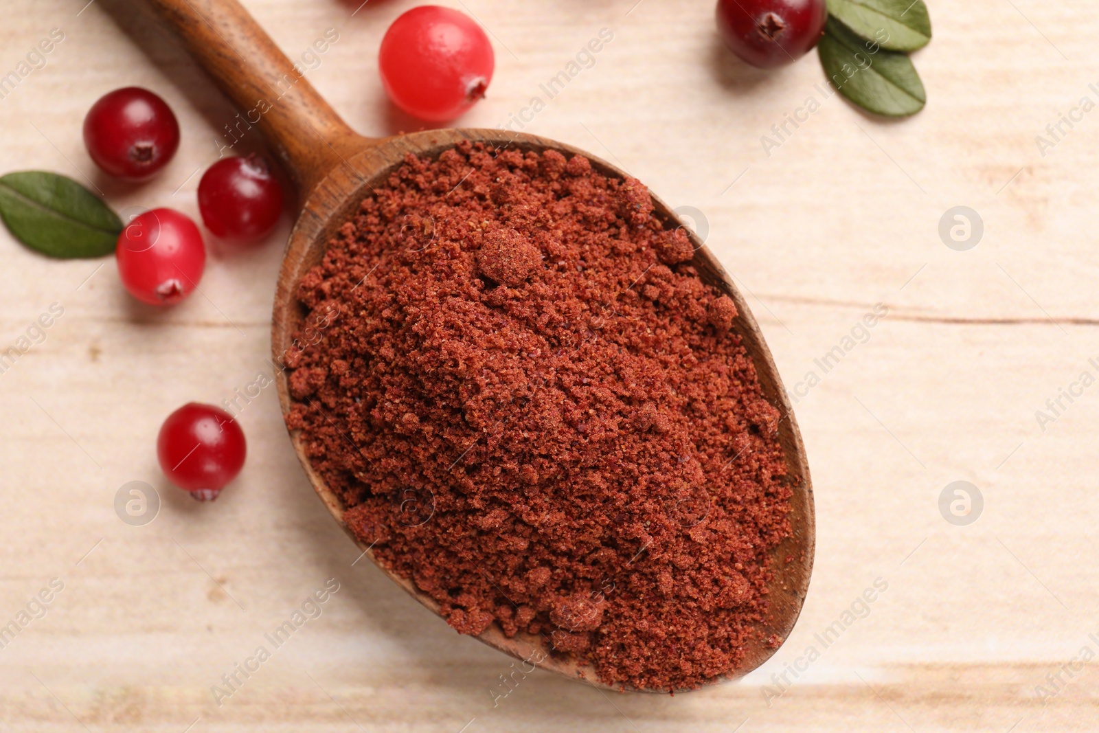 Photo of Dried cranberry powder in spoon, fresh berries and green leaves on light wooden table, top view