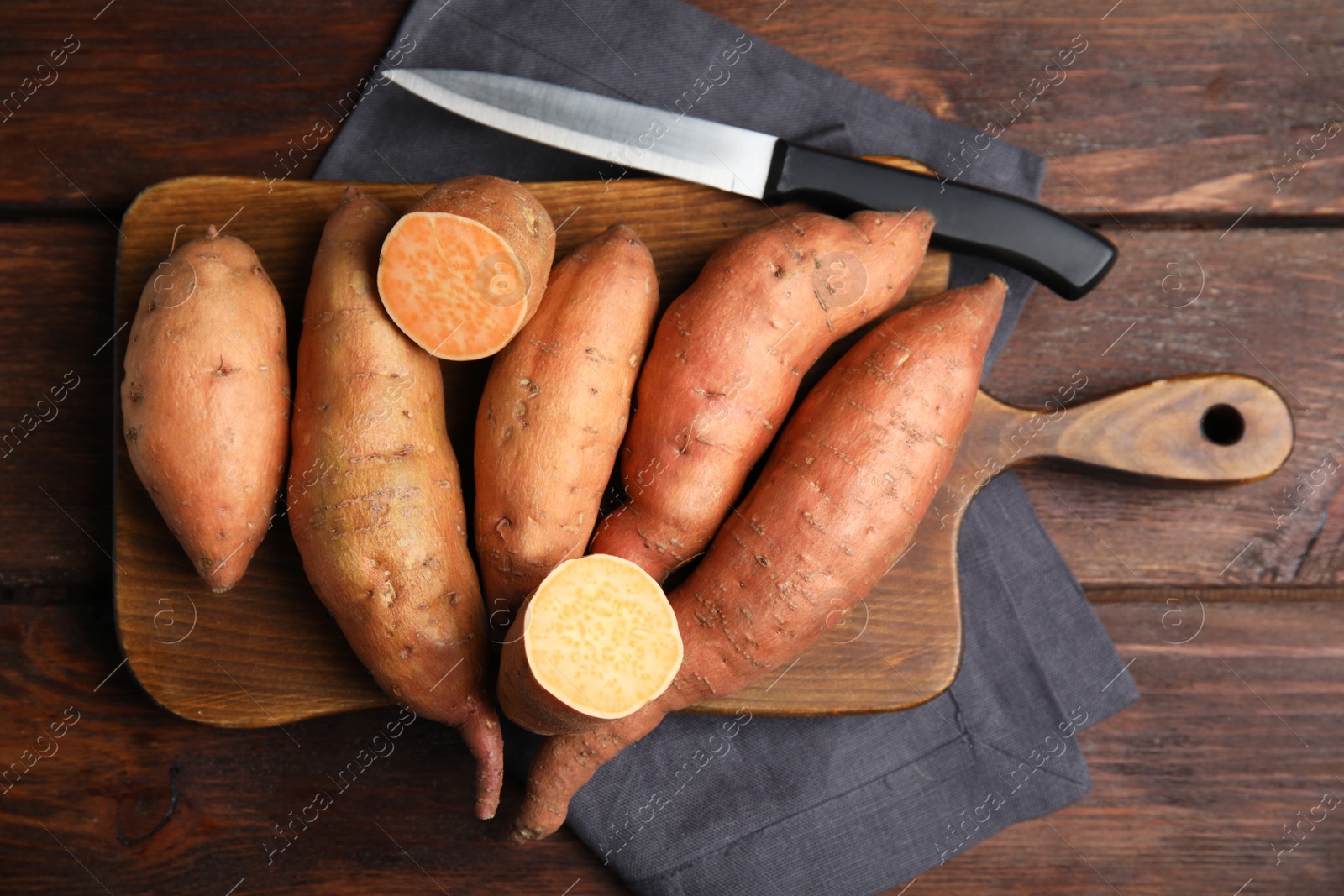 Photo of Whole and cut ripe sweet potatoes on wooden table, flat lay