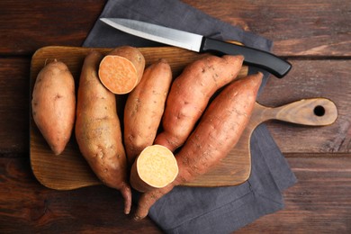 Photo of Whole and cut ripe sweet potatoes on wooden table, flat lay