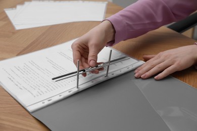 Woman fixing folder with punched pockets at wooden table, closeup