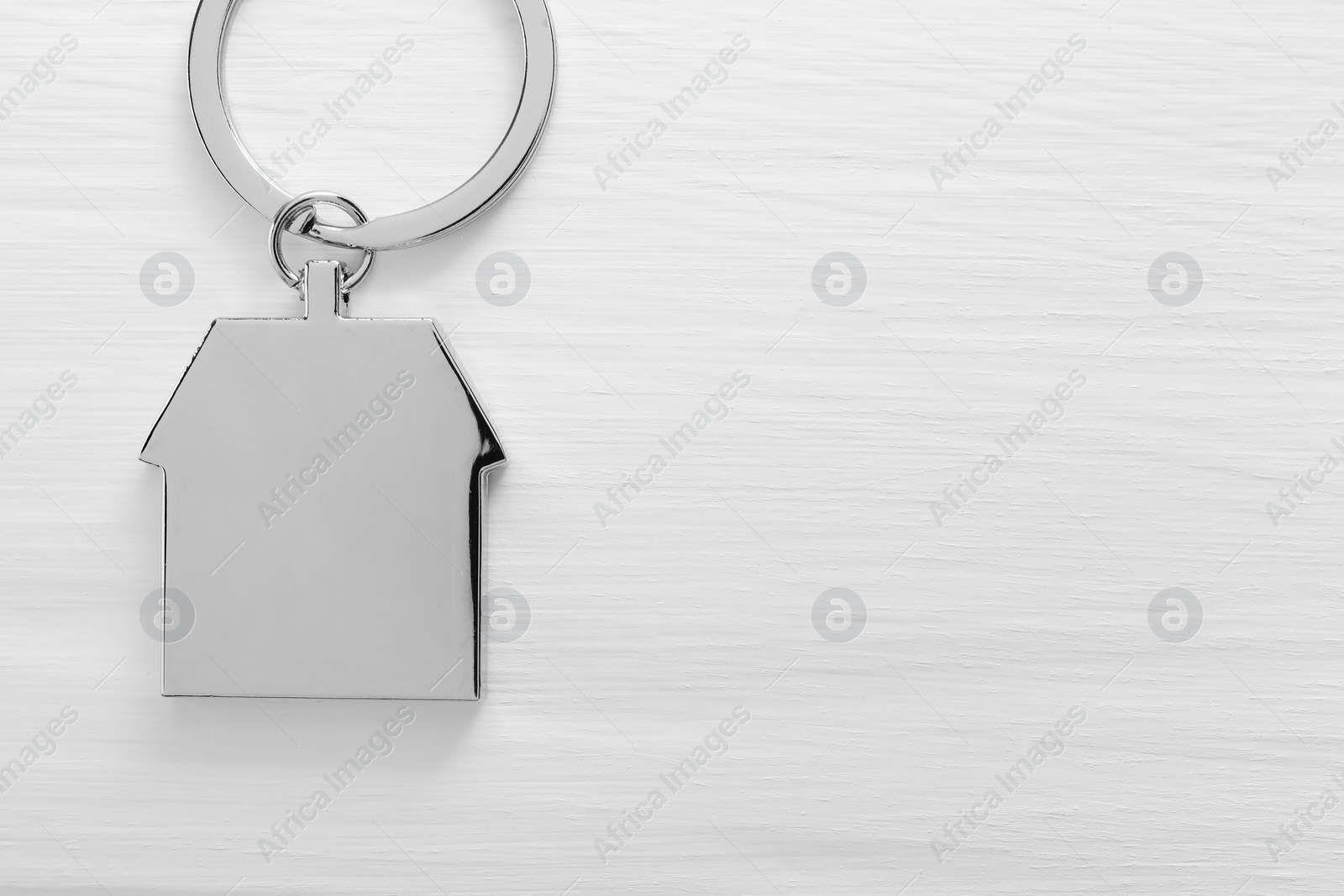 Photo of Metal keychain in shape of house on white wooden table, top view. Space for text