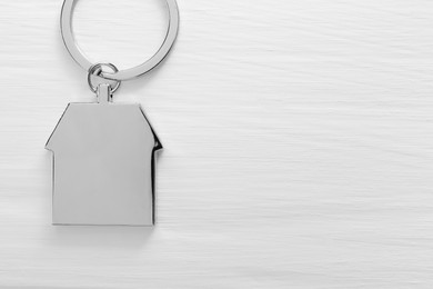 Metal keychain in shape of house on white wooden table, top view. Space for text