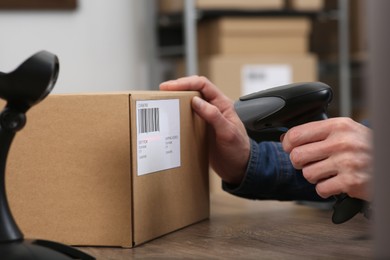 Photo of Seller with scanner reading parcel barcode at table in office, closeup. Online store