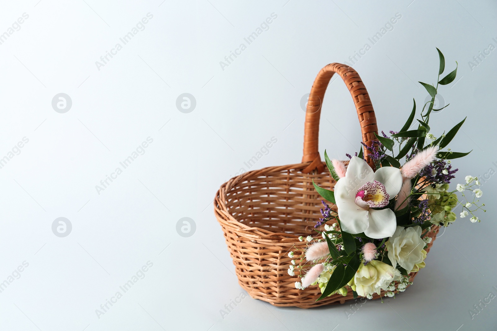 Photo of Wicker basket decorated with beautiful flowers on light background, space for text. Easter item