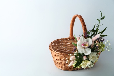 Wicker basket decorated with beautiful flowers on light background, space for text. Easter item