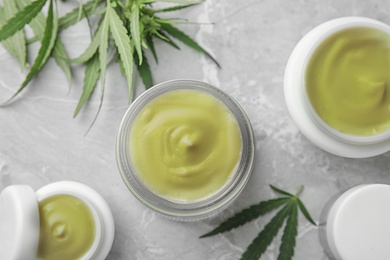 Photo of Jars of hemp cream on grey table, flat lay. Organic cosmetics