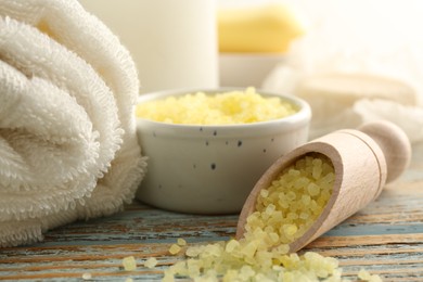 Wooden scoop of yellow sea salt and towel on rustic table, closeup