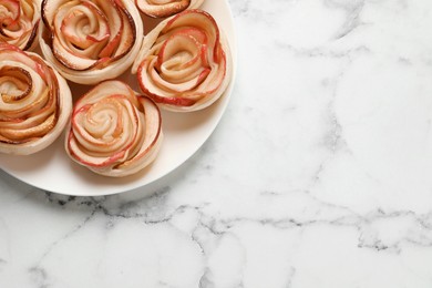 Photo of Freshly baked apple roses on white marble table, top view. Space for text