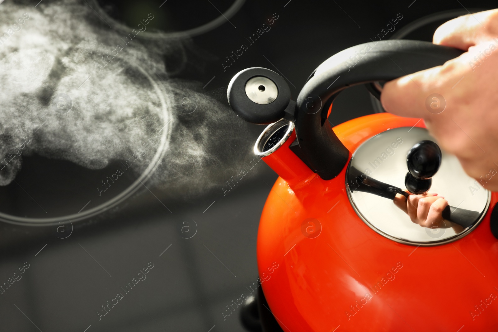 Photo of Woman holding modern kettle on stove, closeup with space for text