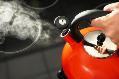 Woman holding modern kettle on stove, closeup with space for text