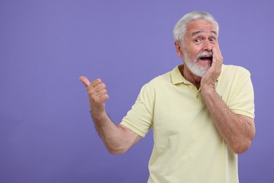 Photo of Special promotion. Emotional senior man pointing at something on purple background. Space for text