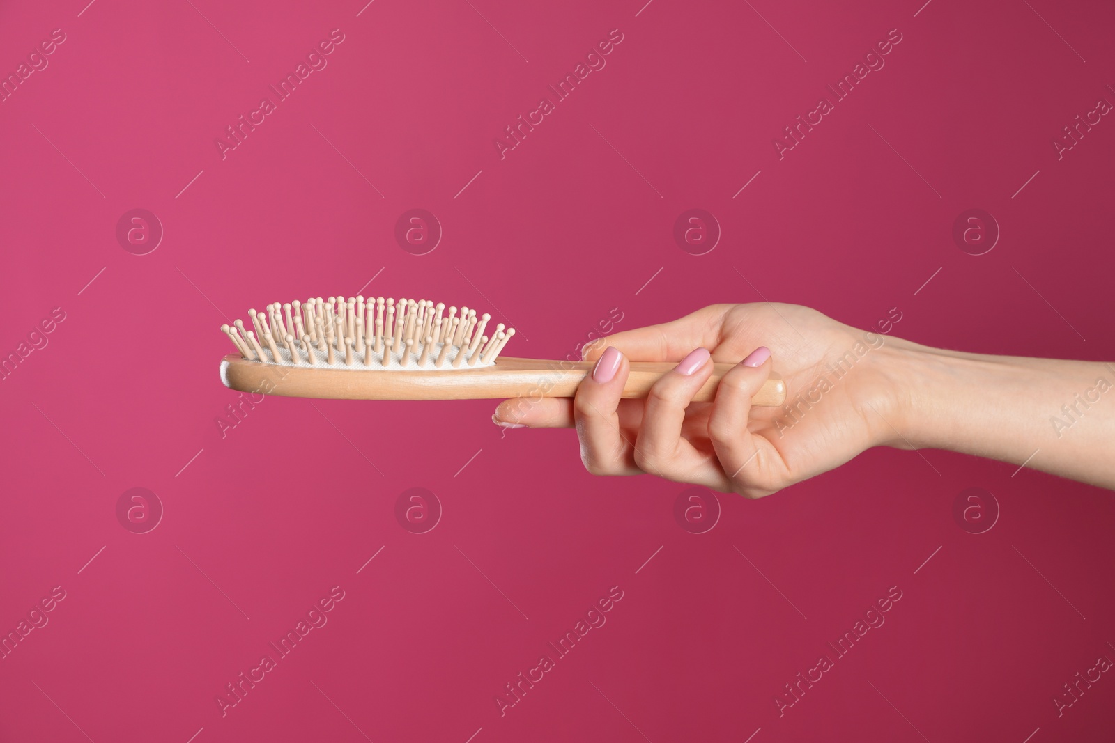 Photo of Woman holding wooden hair brush against crimson background, closeup