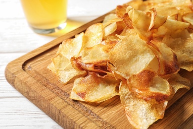 Photo of Wooden board with crispy potato chips on table, closeup