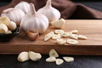 Aromatic cut garlic, cloves and bulbs on dark table, closeup